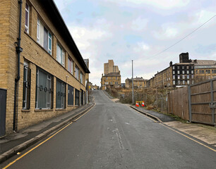 Tetley street rises uphill flanked by old brick buildings with barred windows. The sky is overcast, adding a somber tone to the urban landscape, in the post industrial city of, Bradford, Yorkshire, UK