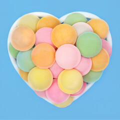 Sherbet UFO flying saucer candy sweets in heart shape dish on blue. Romantic fun multicolored candy treats symbol.