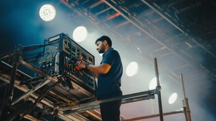 A focused crew member works on soundboards and wiring above a concert stage. Concept of event setup and professional live-show support.