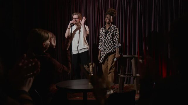 Two stand-up artists ending their performance and going off stage, while everyone applauding, sitting at tables