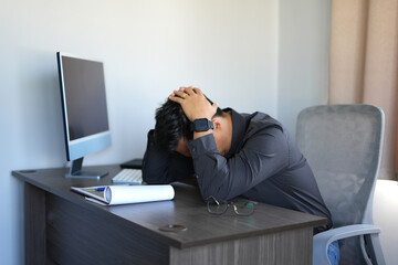 
A young asian man manager working at the office feels headache and sleepy while sitting, calculating and using a laptop for a long time and depression and stress,  health care and medical concept.