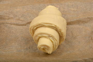 A single, unbaked croissant dough rests on a piece of parchment paper, ready for the oven