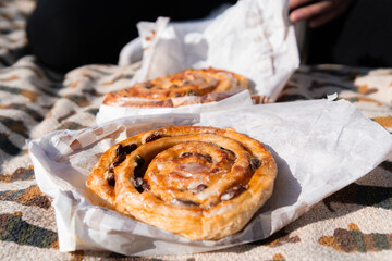 Freshly baked bun on paper wrap during picnic, warm golden crust, casual outdoor food scene in natural light