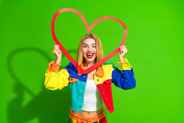 Cheerful Young Woman Posing With Vibrant Heart in Colorful Fashion Outfit Against Bright Green Background