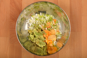 A top-down view shows a stainless steel bowl containing mashed avocado, chopped onions, spices including garlic powder, and yolks, being prepared as a filling for deviled eggs, on a wooden surface