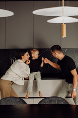 Happy family playing in modern kitchen: parents interacting with son