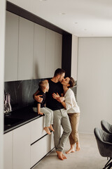 Obraz premium Parents kissing in kitchen while their son sits on the countertop