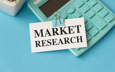 A calculator sits on a blue surface with a white sign that says Market Research
