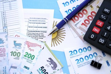 Argentine pesos money bills in big amount lies on table with pen, calculator, passport and tax forms