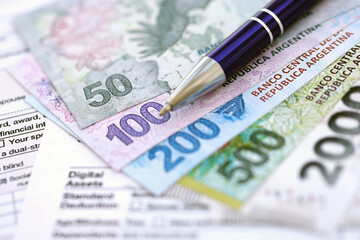 Argentine pesos money bills in big amount lies on table with pen and tax forms close up