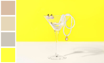 Glass with pearl jewelry on table against yellow background