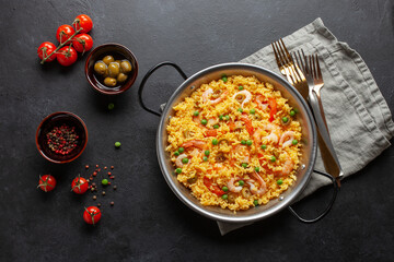 Traditional spanish seafood paella with rice, shrimps, olives and green peas in paellera on the table. Top view