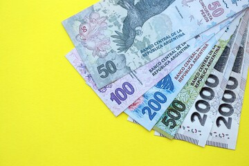 Argentine pesos money bills in big amount lies on yellow color table close up