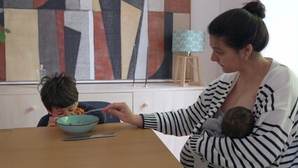 Child expressing reluctance to eat food offered by mother who is simultaneously breastfeeding,...