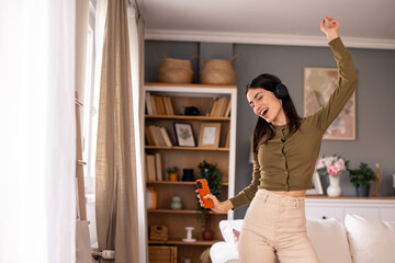 Joyful Woman Dancing in a Cozy Living Room with Headphones and Phone in Hand