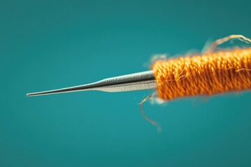 Close-up of a needle threaded with orange yarn against a teal background.