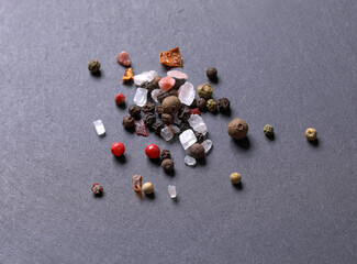 Scattered peppercorns mix with some salt crystals on a gray background. Small pile of spice mix top view. 