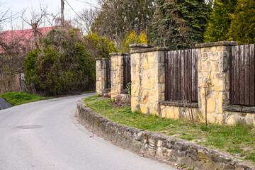 a winding asphalt road running along a stone fence with wooden sections. The fence consists of pillars made of light roughly processed stone
