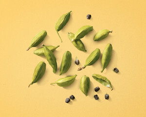 Cardamom pods and seeds scattered on pastel yellow background, top view.