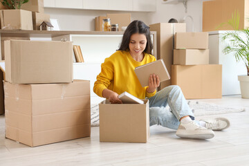 Beautiful woman packing books into box in kitchen on moving day