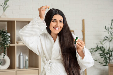 Young pregnant woman applying serum for hair growth in bathroom
