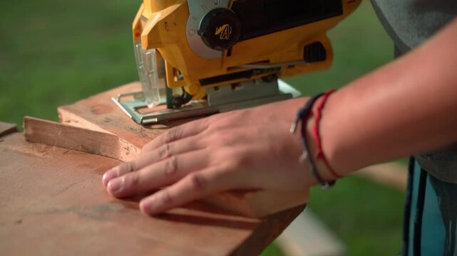 Close-up of young man cutting curved shape in wood with jigsaw in an outdoor carpentry setup