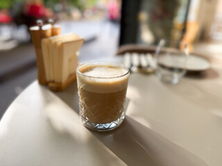 Hot coffee served in a low crystal glass stands on a white table in a city cafe. Breakfast moments and urban coffee culture.