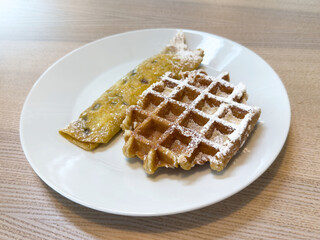 Delicious plate of crepe and waffle with powdered sugar on a wooden table