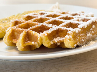 Close-up of powdered sugar belgian waffle on white plate