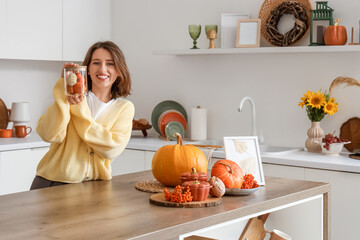 Pretty young woman with pumpkins, berries and autumn decorations in light kitchen