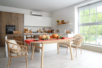 Interior of light kitchen with autumn decor, pumpkins and dining table