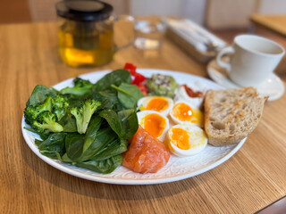 Healthy breakfast plate with vegetables, eggs and salmon served with herbal tea. Balanced nutrition and clean eating in a modern cafe