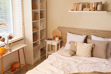 Interior of modern bedroom with comfortable bed, pillows and pumpkins on bedside tables