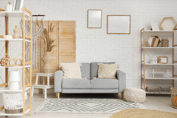 Interior of light living room with grey sofa, pampas grass and shelving units