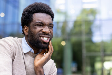Man suffering from toothache. African American businessman sitting on a bench outside an office...