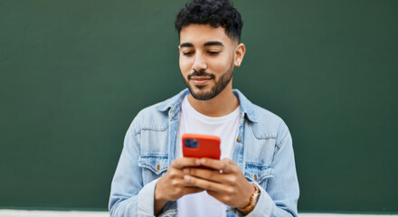 Young hispanic male using smartphone outdoors in casual denim jacket