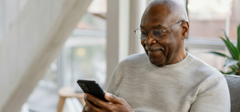 Elderly african male relaxing at home using smartphone, enjoyment and technology indoors