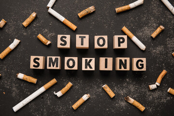 Composition with text STOP SMOKING made of wooden cubes and cigarette butts on dark background