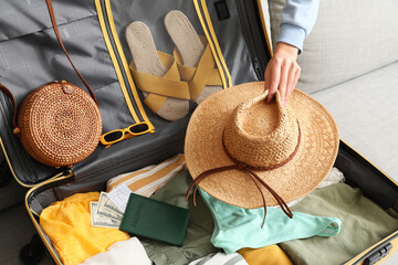Young woman with hat packing suitcase for travel on sofa at home, closeup