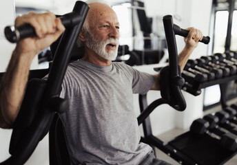 Older man using fly machine for training in gym