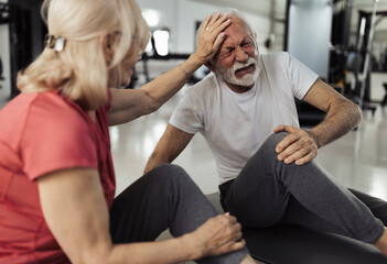 Fototapeta premium Older lady comforting man after injuring leg in gym