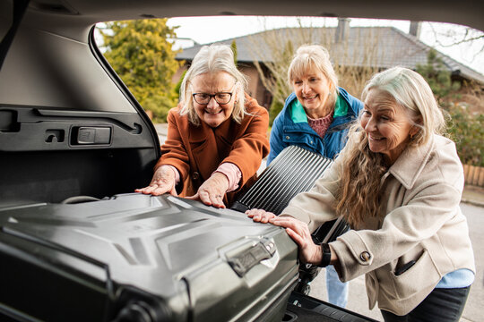 Senior women friends packing their suitcases into a trunk of a car before going on a road trip vacation