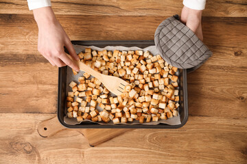 Young woman and baking tray with prepared croutons on wooden background