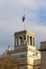 View of a government building with a flag atop, featuring classical architecture and statues. The...