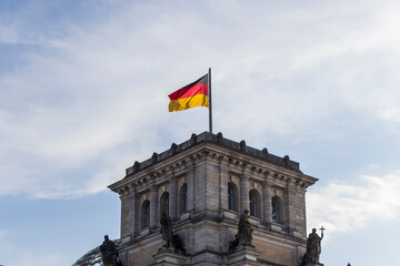 The German flag waves proudly atop the Reichstag building in Berlin under a bright blue sky. This...