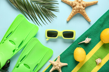 Beach towel with flippers, sunglasses and palm leaf on blue background