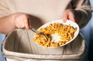 Woman holding food plate and throwing away food leftovers using spoon into garbage bin trash....