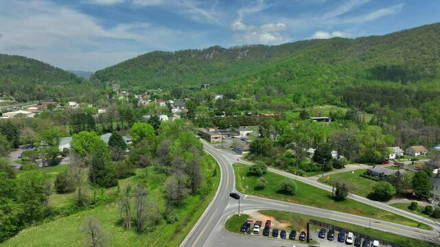 Aerial flyover street of small american town between green growing hills in spring. Lovingston Town, Virginia, USA. Industrial area with garages and houses along main suburb road.