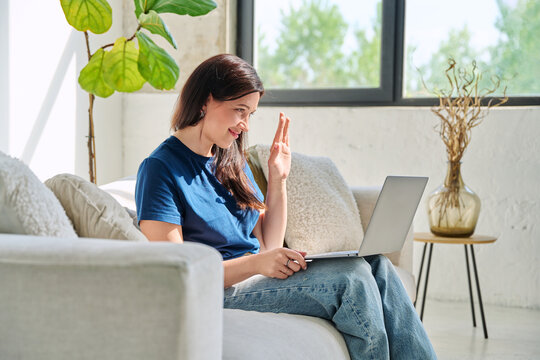 Young woman looking at laptop screen talking having video call sitting on couch at home