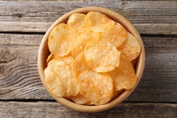 Tasty potato chips in bowl on wooden table, top view